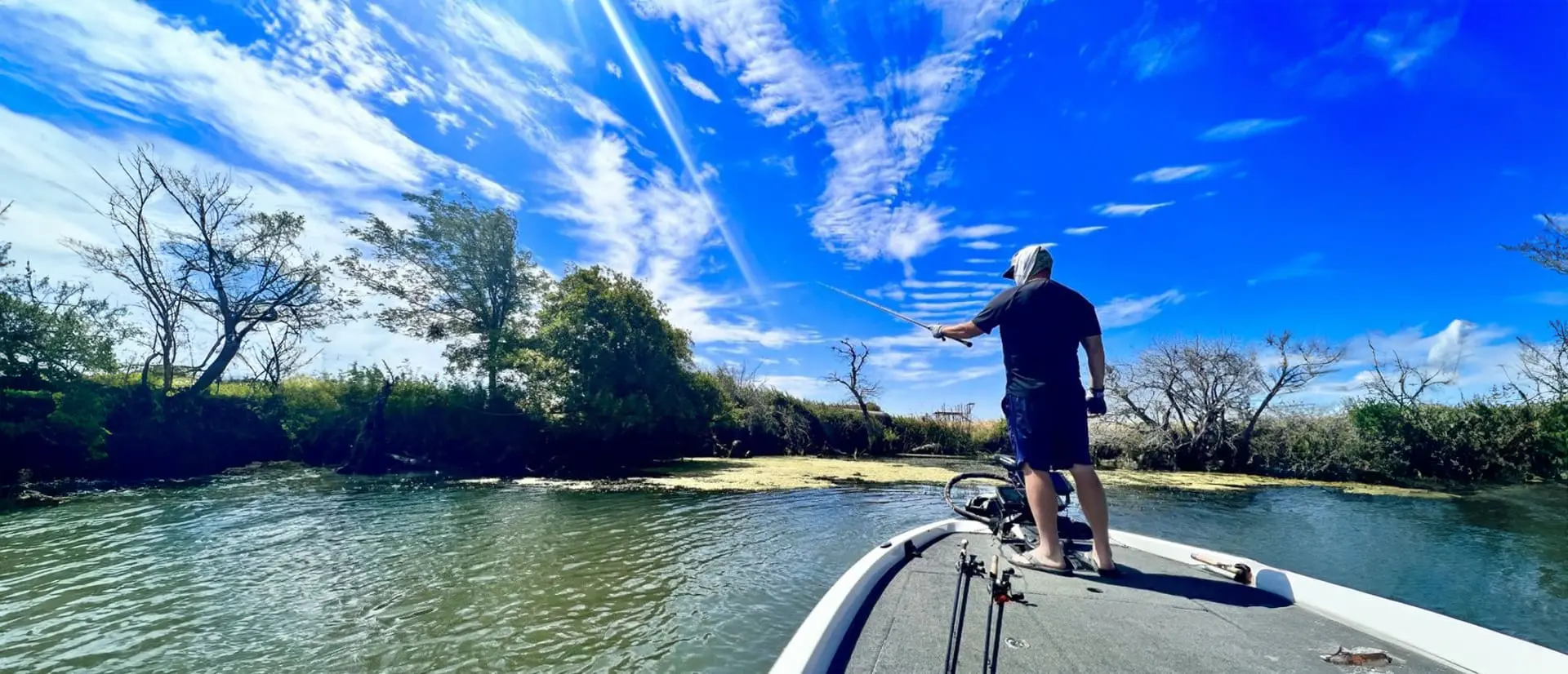 A man standing on the back of a boat in water.