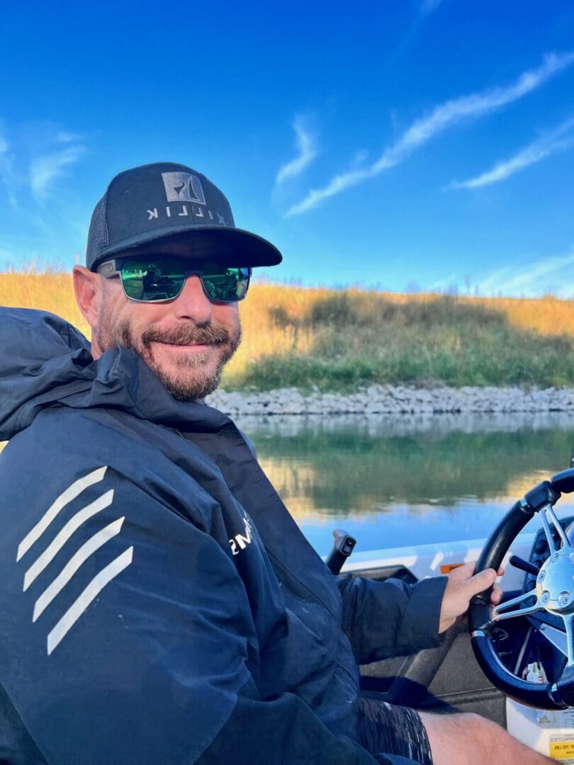 A man in a hat and sunglasses is sitting on the boat.